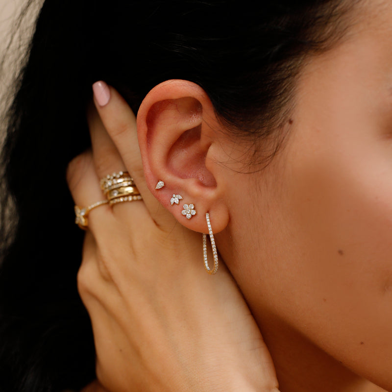 Model with multiple piercings wears solid gold 14k wavy hoop lined in diamonds with other handmade diamond studs
