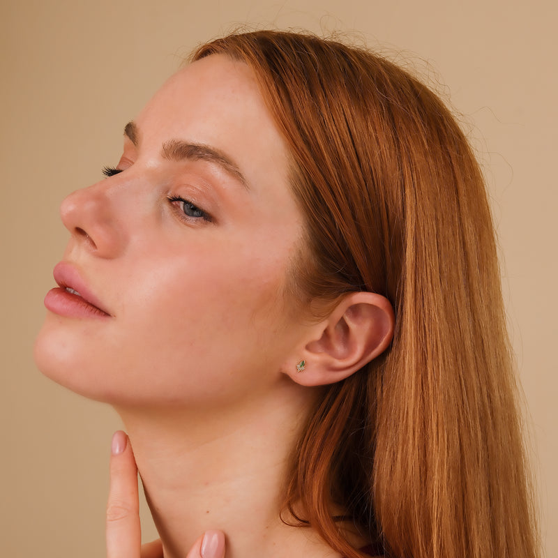 Model wears dainty marquise green emerald studs with three diamonds
