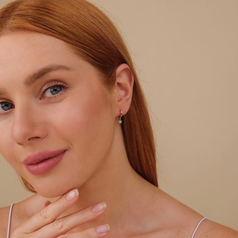 Model wears solid 14k gold white diamond star shaped hoop huggies