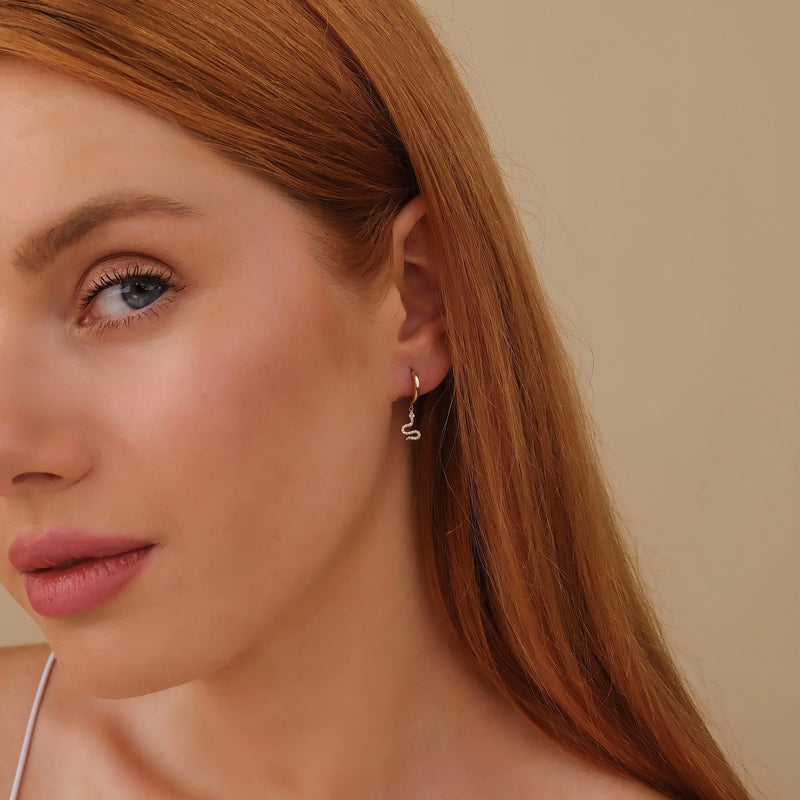 Model wears minimalistic white diamond huggies in snake shape