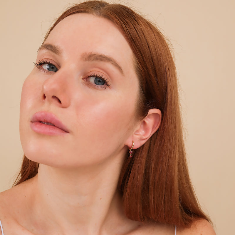 Model wears solid 14k gold huggies with two hanging rubies