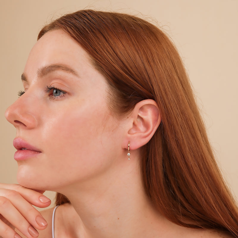 Model wears minimalist solid 14k gold huggies with two hanging diamonds