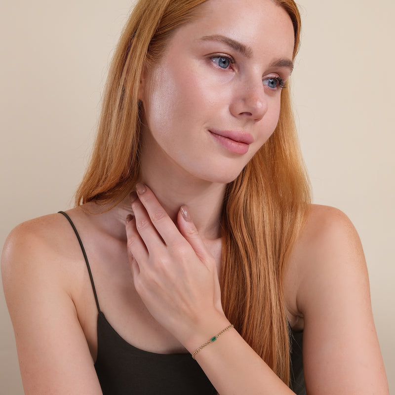 Gold Cuban link bracelet with a single emerald in a bezel setting