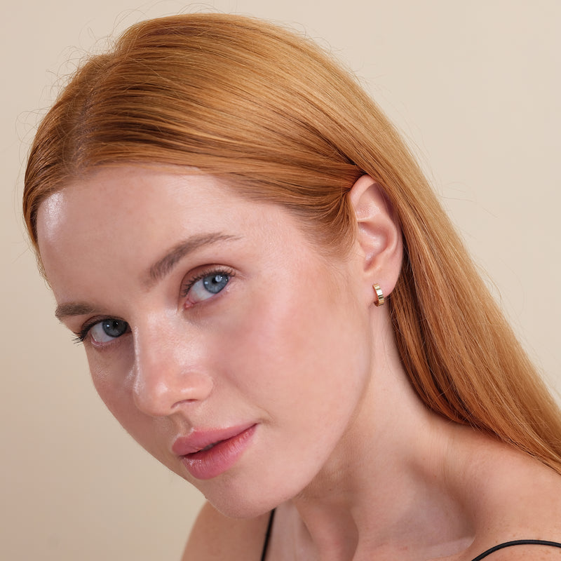 Model wears solid 14k gold fluted pattern simplistic hoop huggie. 