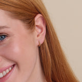 Model wearing dainty 14k solid gold twisted huggie hoop earring. 