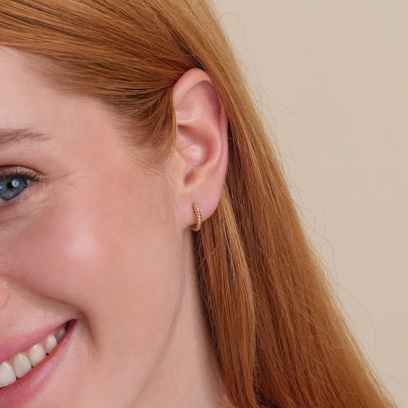 Model wearing dainty 14k solid gold twisted huggie hoop earring. 