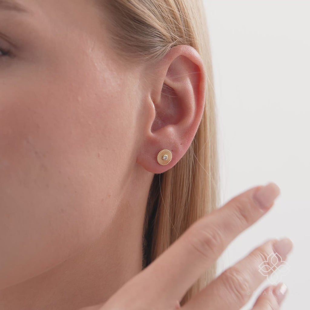 Thia Infuse your style with the radiant energy of our Sunburst Diamond Studs. These exquisite earrings are meticulously crafted from lustrous solid gold, featuring a unique circular motif with deeply engraved sunburst lines radiating outward. At the cente