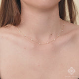 Model wearing a gold natural pearl station necklace, layered with other delicate necklaces.