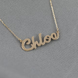 Close-up of a dainty cursive name pendant in solid gold on a gold chain.