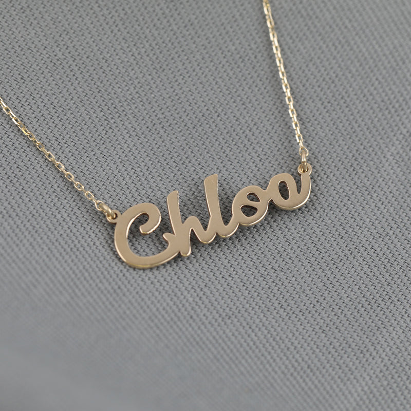 Close-up of a dainty cursive name pendant in solid gold on a gold chain.