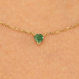 Close-up of a vibrant green emerald heart pendant in a gold setting.