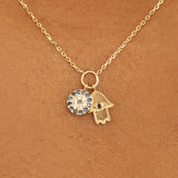 Close-up of a blue sapphire Evil Eye charm and a diamond-studded Hamsa charm with a delicate gold chain.