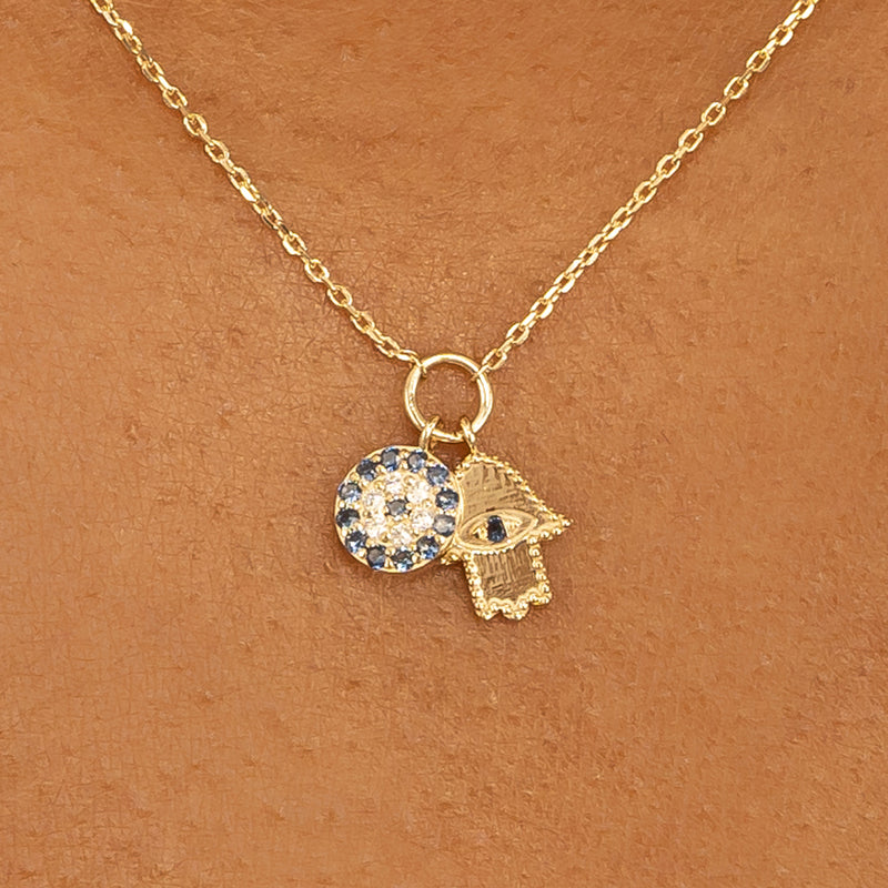 Close-up of a blue sapphire Evil Eye charm and a diamond-studded Hamsa charm with a delicate gold chain.