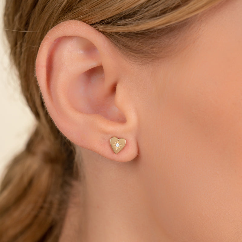 Model wears gold 14k white gold stud earring in heart shape with single diamond