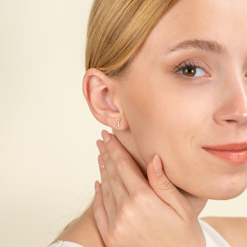 Model wears 14k solid gold diamond earring stud in key and heart shape 