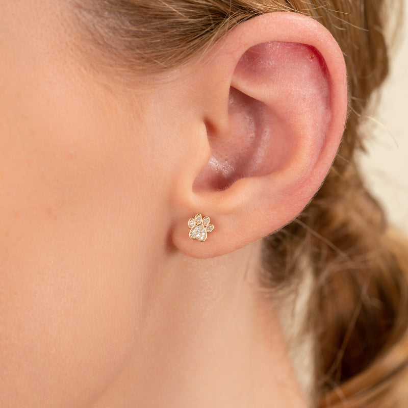 Model wears dainty handmade dog paw stud earring with paved diamonds